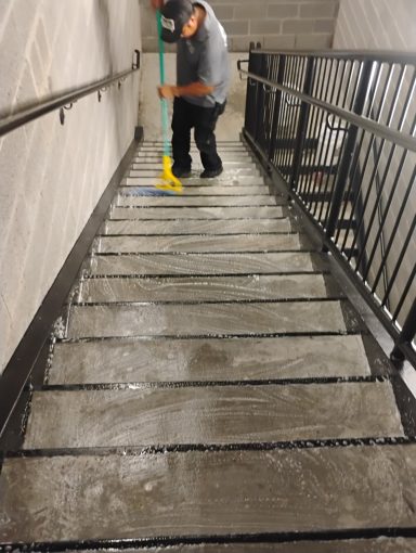 Persona limpiando escalones con un trapeador en un entorno interior.